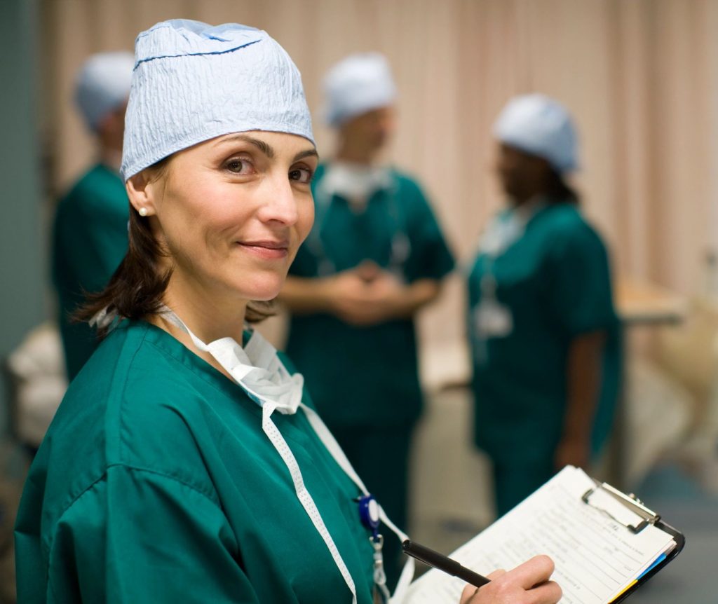 Female health professional in operation scrubs holding clipboard.