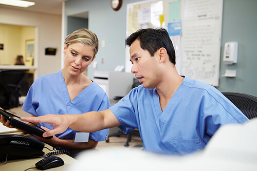 Two nurses at station looking at computer.